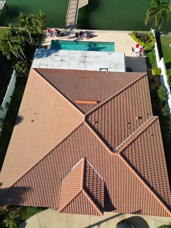 Aerial view of a completed terracotta tile roof on a waterfront Florida home with a pool